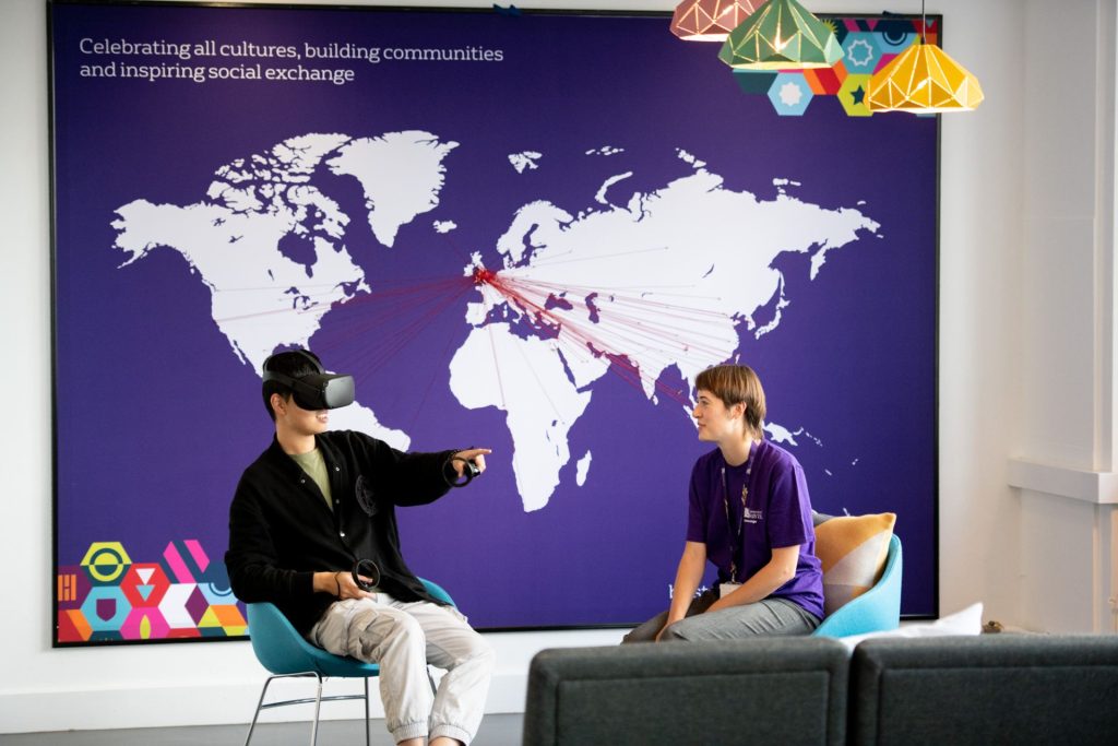 Person uses a VR headset in the Global Lounge, while another watches. 